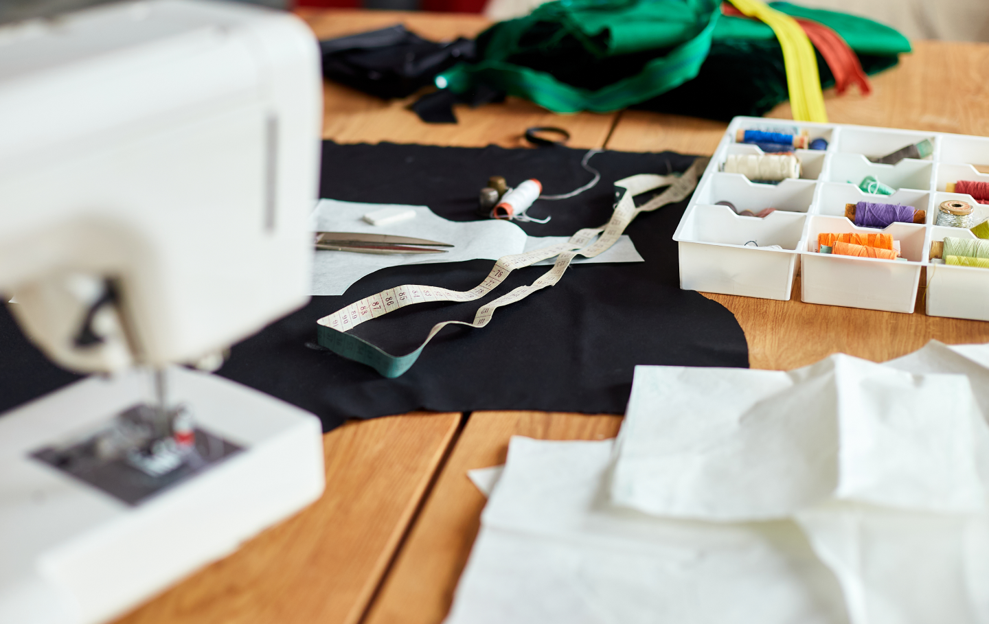 Sewing setup with fabric, sewing machine, threads, measuring tape, and scissors on a wooden table.