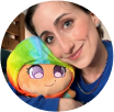 A person smiling while holding a colorful stuffed toy.