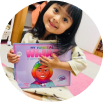 A young girl smiling and holding a colorful children's book.