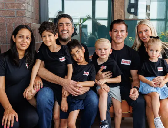 A diverse group of adults and children wearing matching black shirts, sitting together and smiling.