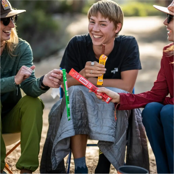 Friends laughing and sharing snacks while sitting outdoors.