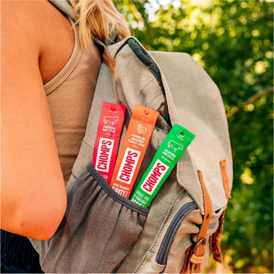 Backpack pocket holding three Chomps meat sticks outdoors.
