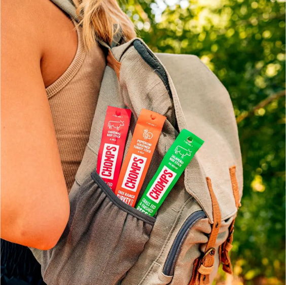 Backpack with three Chomps meat sticks in an outer pocket, worn by a person outdoors.