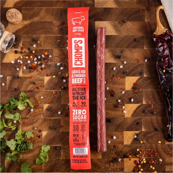 Chomps beef stick on a wooden board with spices and herbs.