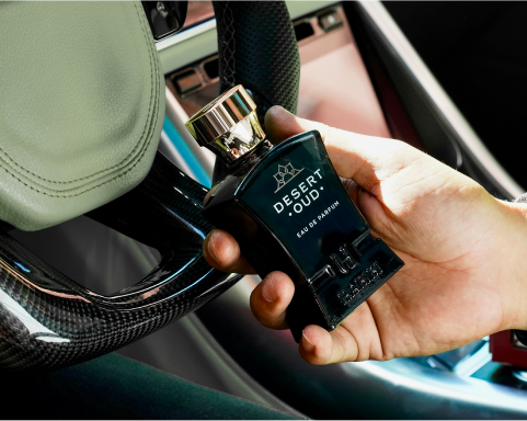 Hand holding a perfume bottle labeled 'Desert Oud' inside a car.