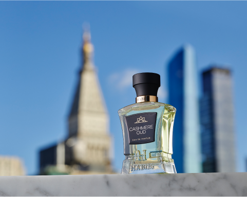 Perfume bottle with skyscrapers in the background against a clear blue sky.