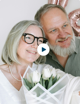 An older couple smiling together, holding a bouquet of white tulips.