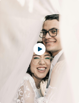 A joyful couple smiling under a sheer fabric, wearing glasses and embracing.
