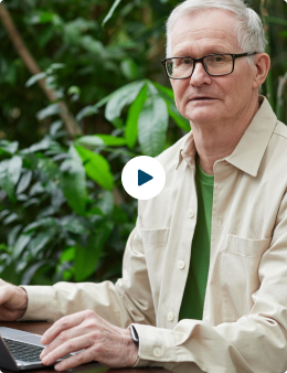Senior man using a laptop outdoors, surrounded by greenery.