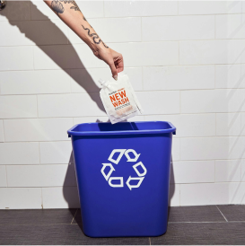 Hand recycling a packet into a blue recycling bin with a symbol.