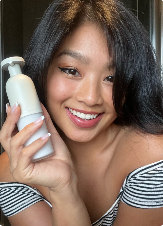 Person smiling, holding a white bottle, wearing a black and white striped top.