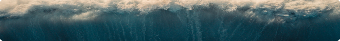 Aerial view of an ocean wave cresting, capturing foam and deep blue water below.