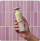 Hand holding a beige ceramic bottle against a pink tiled background.