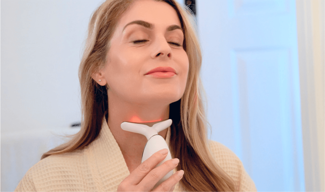 Woman using a skincare device on her neck in a bathroom.
