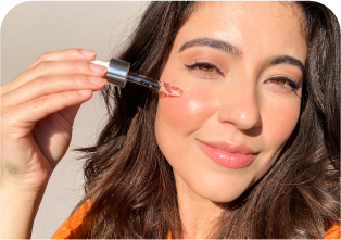 A woman applies facial serum with a dropper on her cheek.