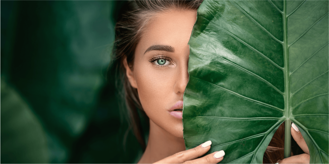 Woman peeking from behind a large green leaf.