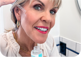 Woman applying skincare serum with dropper in bathroom.
