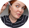 Person applying skincare serum to face with a dropper.