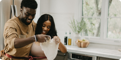 A smiling couple is making pizza dough together in a bright kitchen.