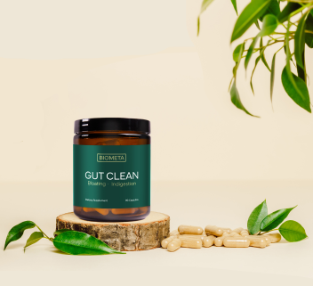 Jar of gut health capsules on a wooden platform with leaves around.