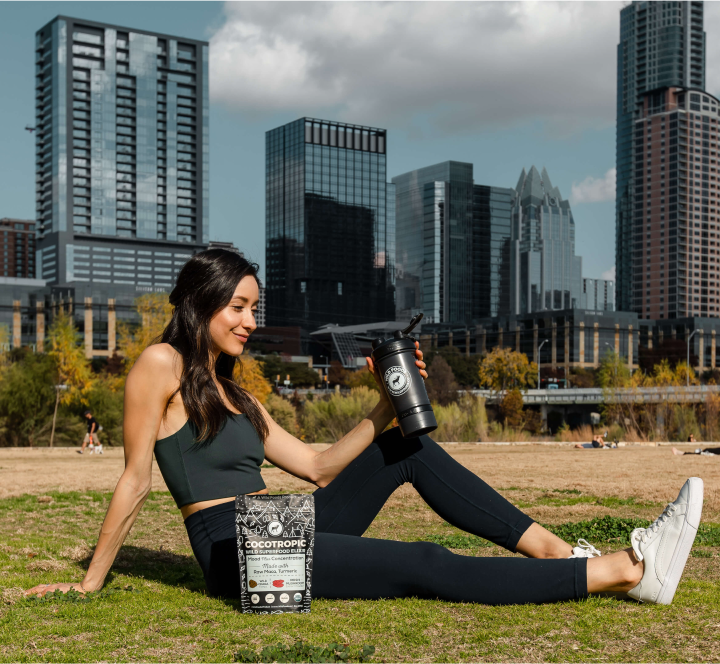 Woman relaxing in a park with a shaker bottle, city skyline in background.