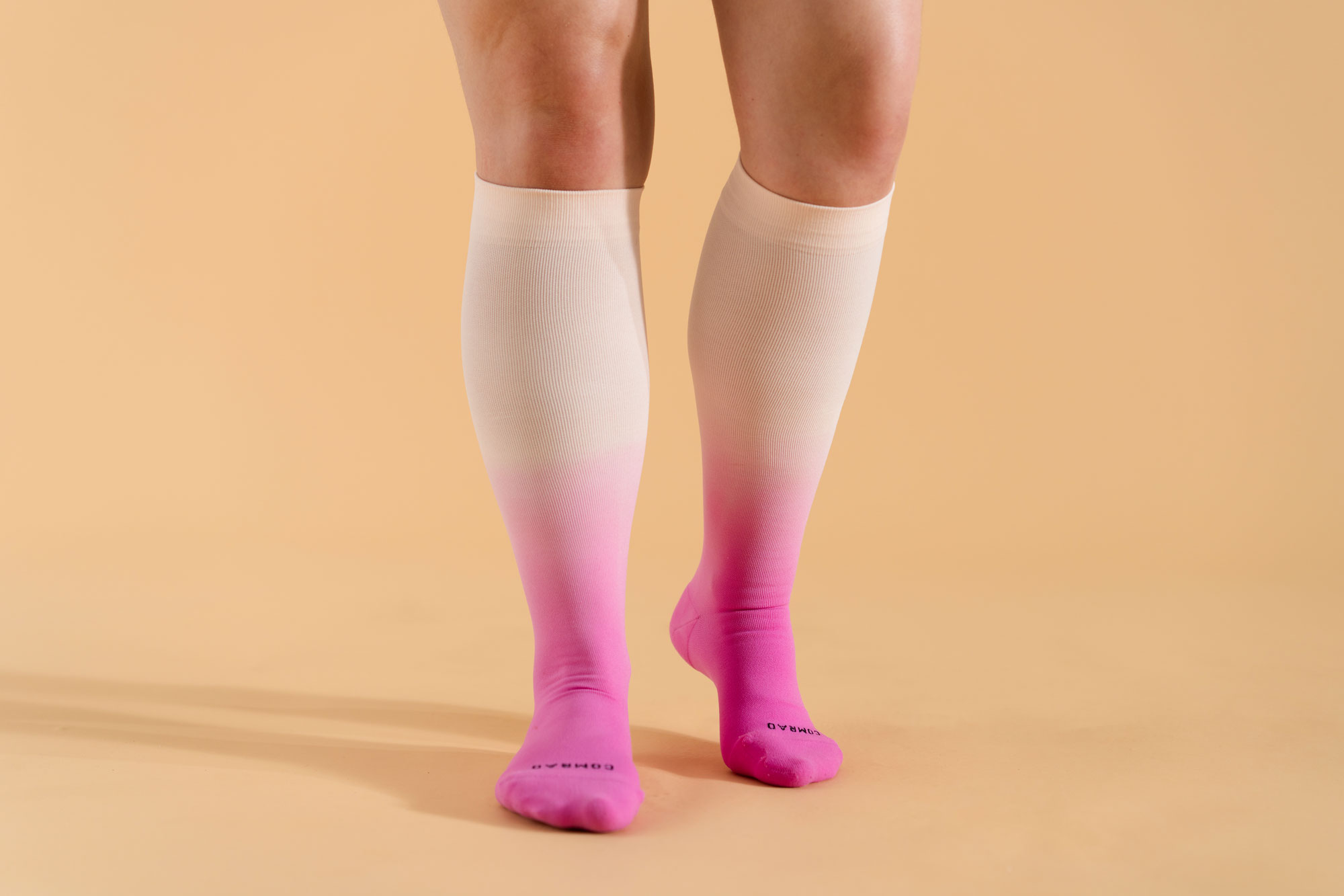 Person wearing knee-high gradient pink socks on a beige background.
