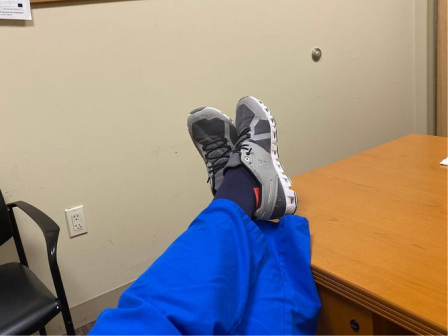 Nurse in blue scrubs resting her feet on a break room table in compression socks and sneakers