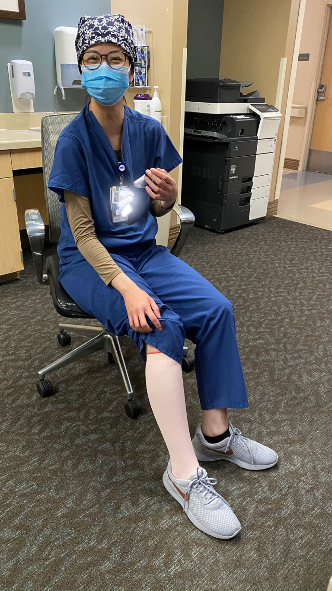 Person in scrubs and mask sitting in an office chair, holding a small object.