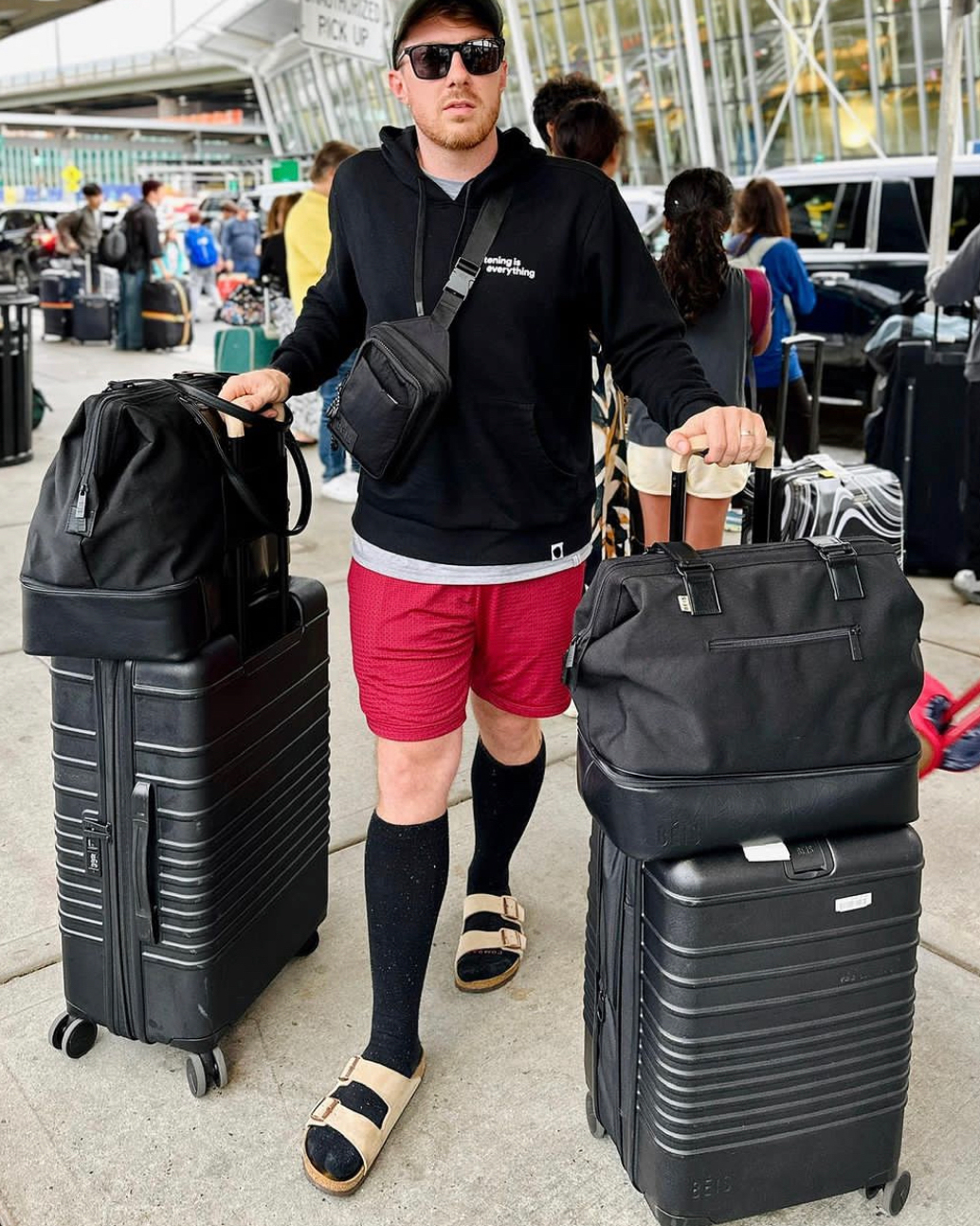 Person at airport with luggage, wearing sunglasses and casual attire.