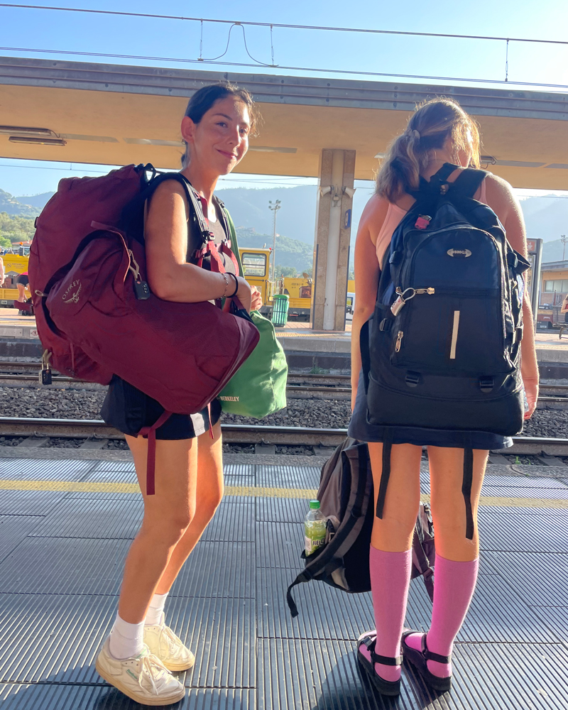Two people with backpacks standing on a train platform.