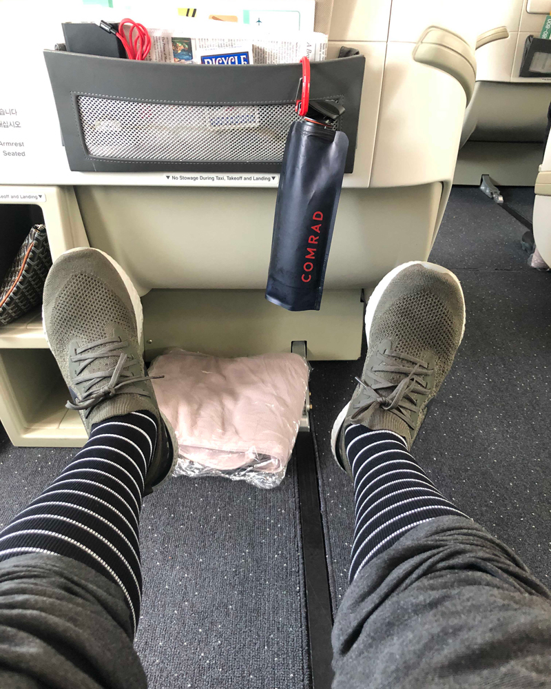 Person wearing striped socks and sneakers on an airplane, with a bag and magazines visible.