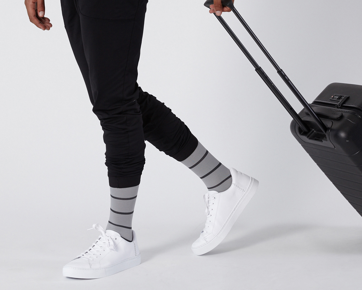 Person in black pants and striped socks pulling a suitcase.