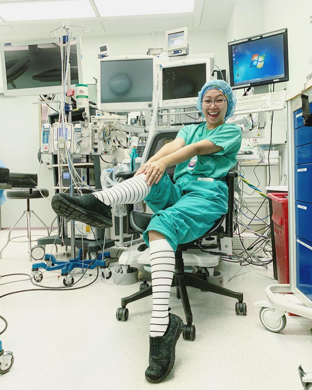 Person in scrubs and striped socks sitting in a medical room with equipment.
