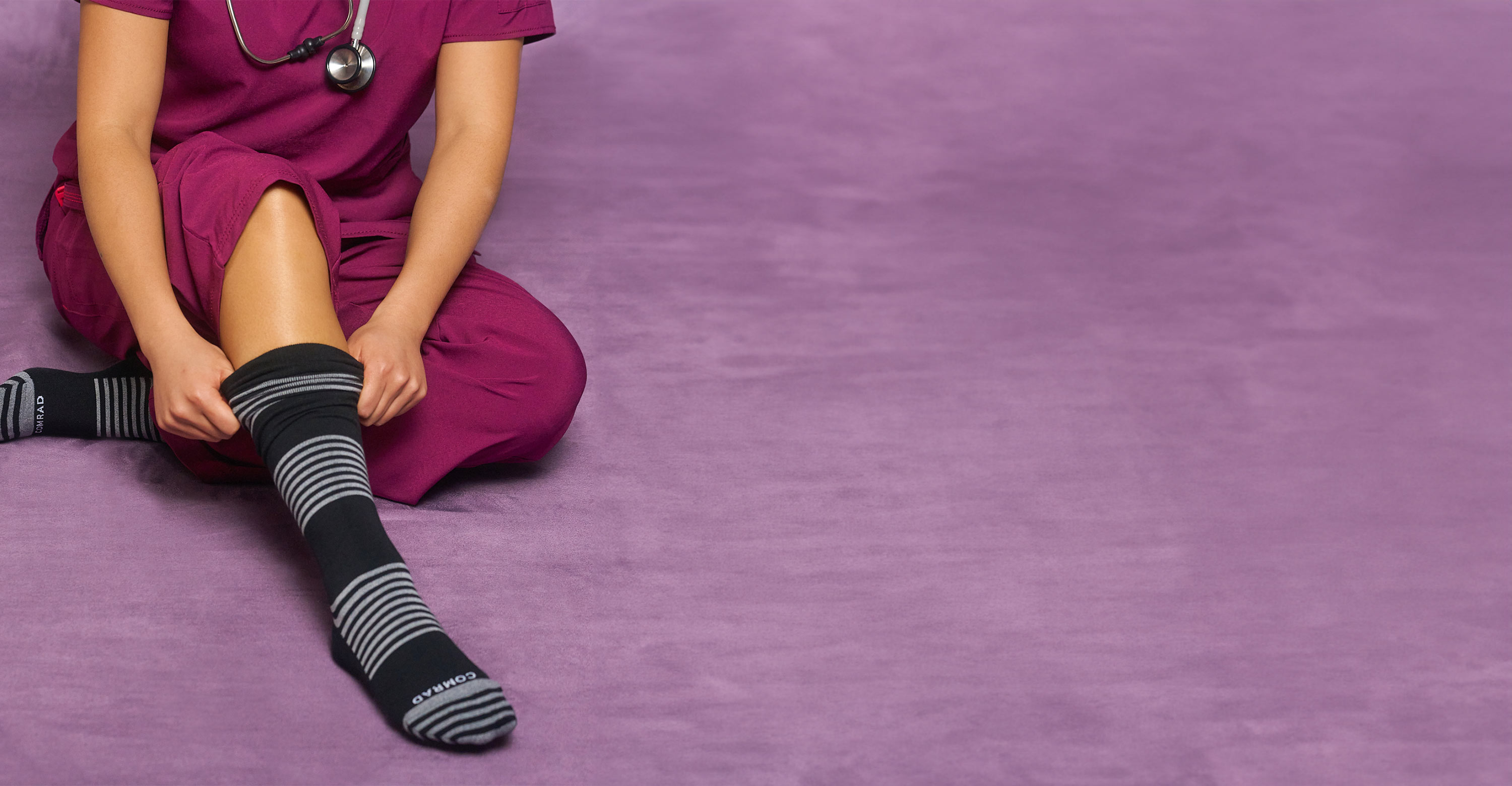 Person in purple scrubs putting on striped socks.