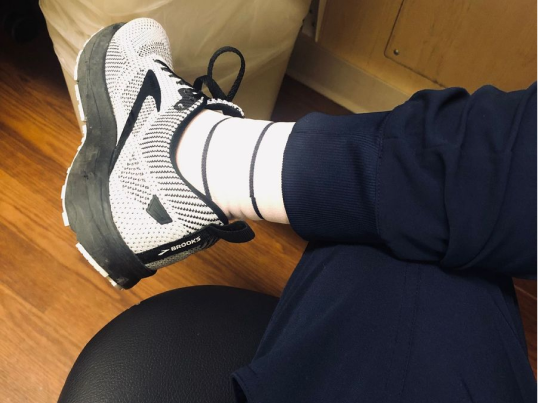 Seated healthcare worker in navy scrubs wearing white striped compression socks with sneakers