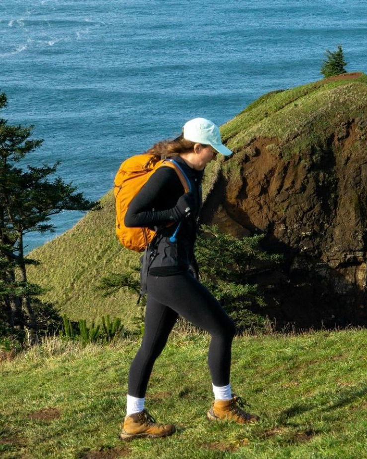 Person hiking on a grassy cliffside with ocean in the background.