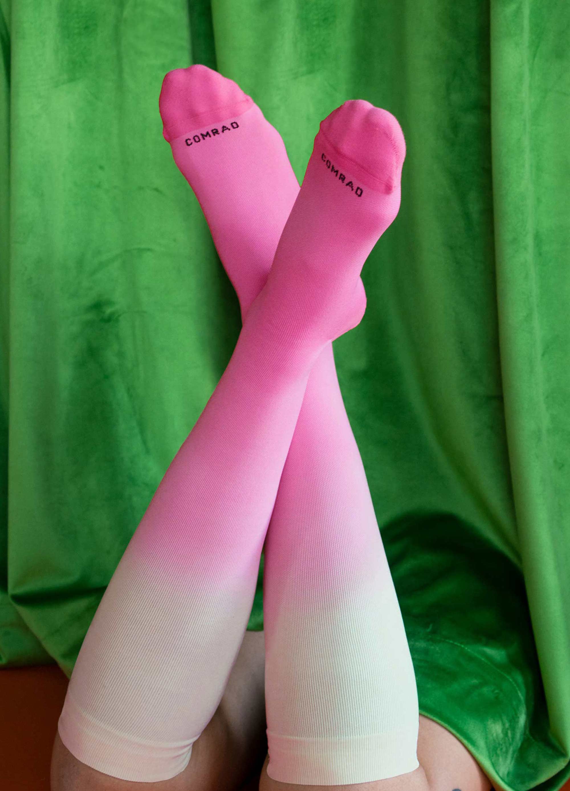 Pink gradient knee-high socks on crossed legs, green background.