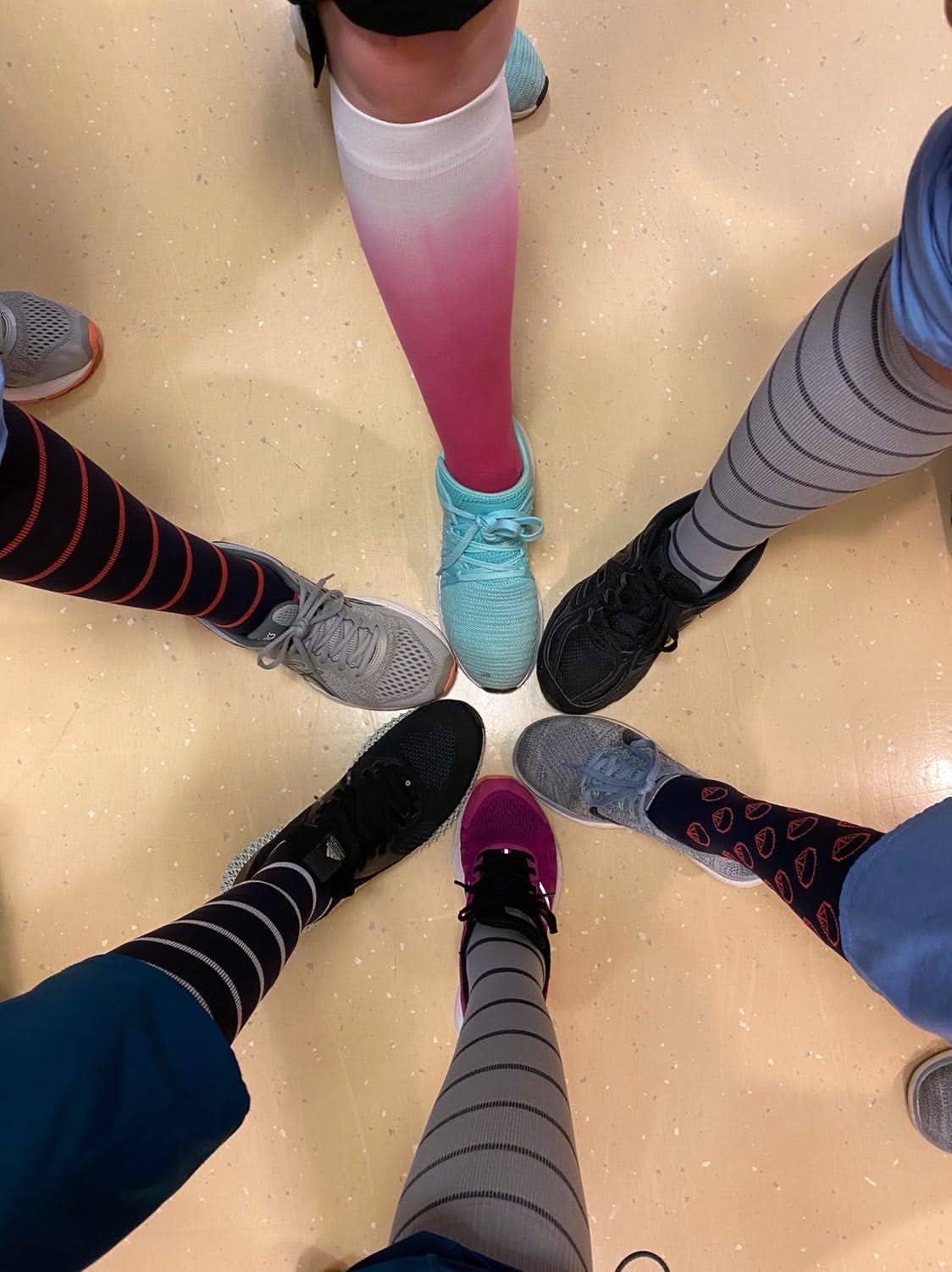 Six people in colorful socks standing in a circle, feet touching in the center.
