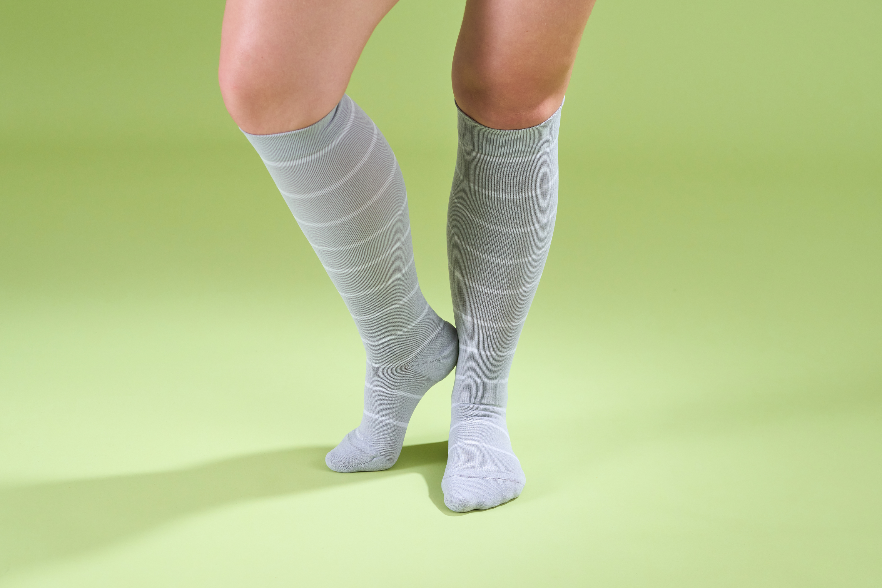 Person wearing gray knee-high socks on a green background.