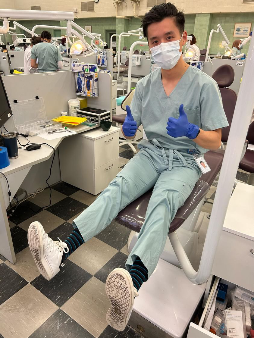 Person in scrubs and mask giving thumbs up in a dental clinic.