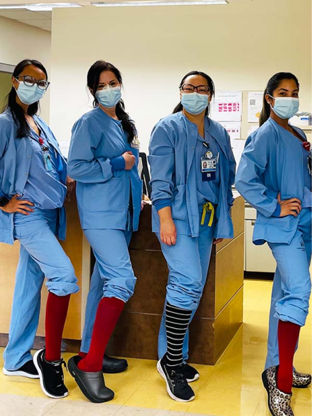 Four nurses in blue scrubs and face masks at a hospital nurses' station, wearing colorful knee-high compression socks