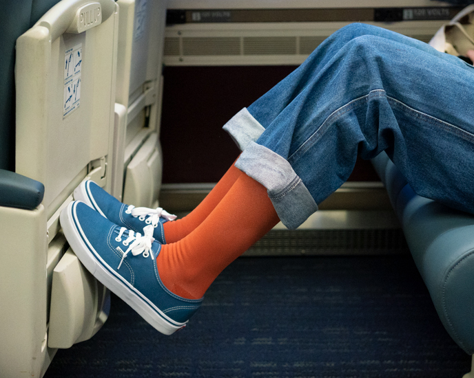 Person wearing orange socks and blue shoes on a train seat.