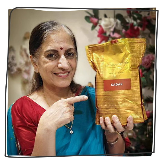 A smiling woman in a sari holds and points to a gold pouch of Kadak chai.