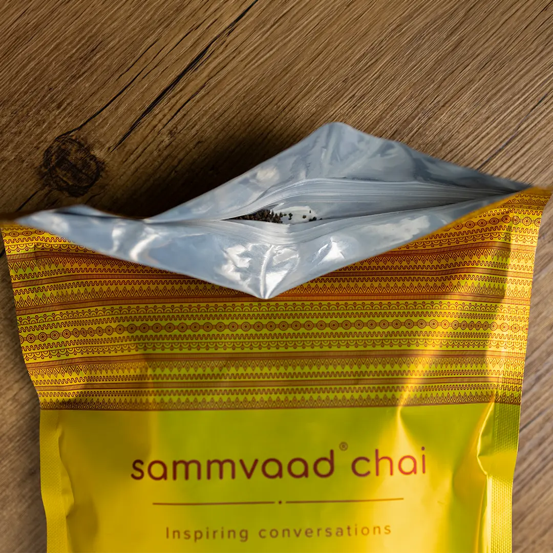 An open yellow pouch of Sammvaad Chai tea, with loose tea visible, on a wooden surface.