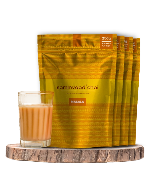 A glass of masala chai with packages of Sammvaad Chai behind it.