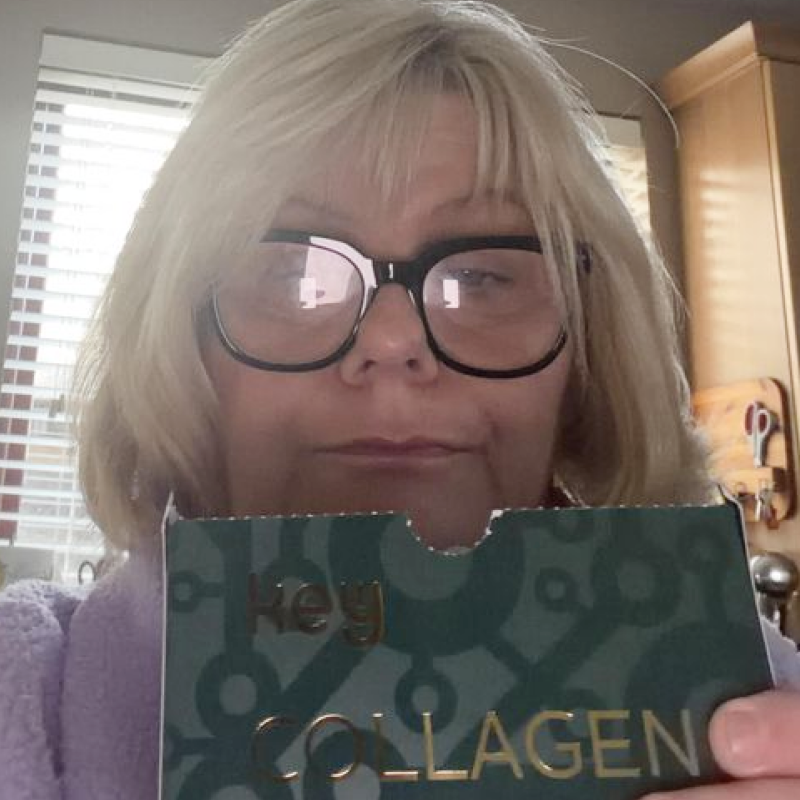 A woman with blonde hair and black-framed glasses holds up a box of Key Collagen.