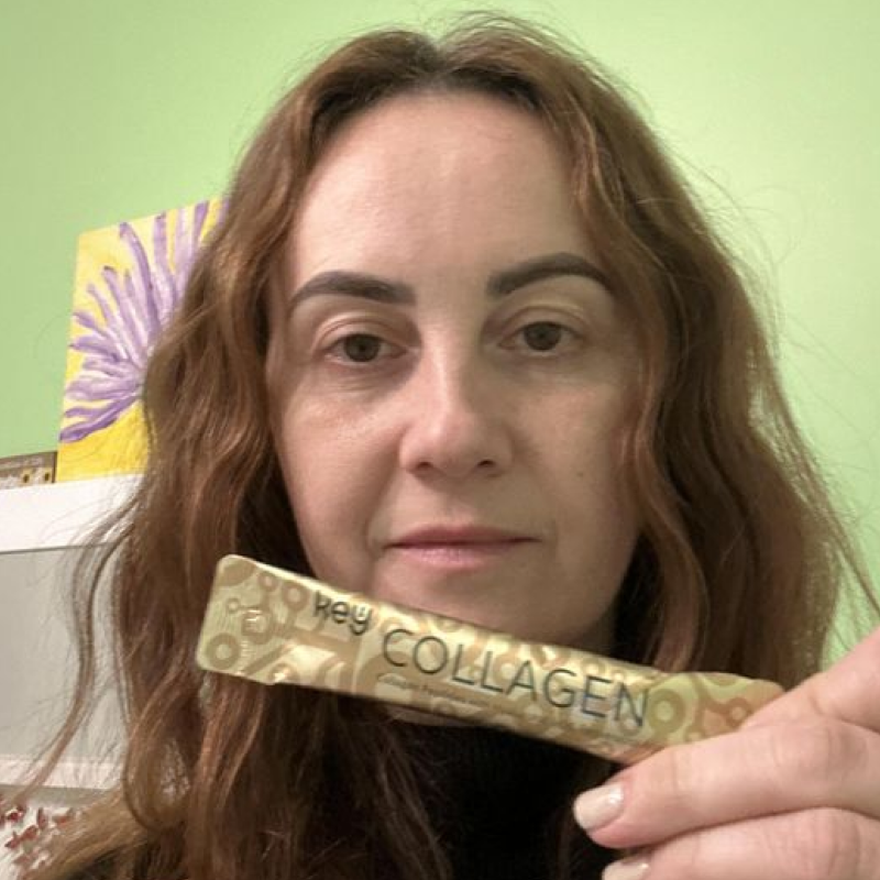 A woman with long, reddish-brown hair holds a gold packet that says 'Key COLLAGEN' towards the camera.