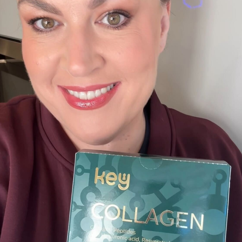 A smiling woman with makeup holds up a green box of Key Collagen.