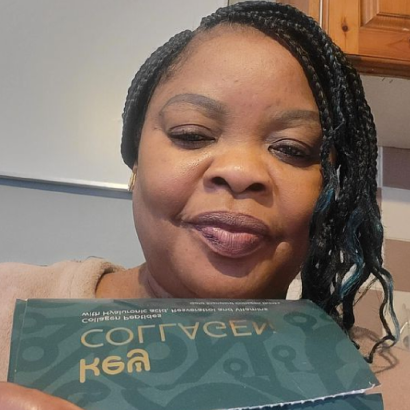 A woman with braided hair smiles while holding up a green box.