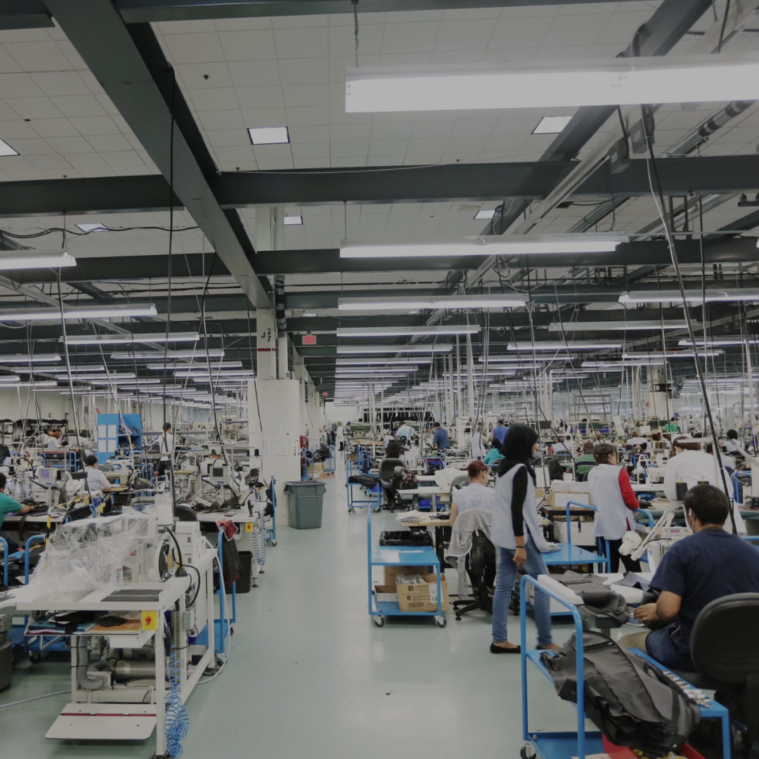 A wide shot of a brightly-lit factory floor with dozens of workers at their stations.